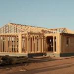 New build house frame with timber trusses on a suburban block with a dirt driveway