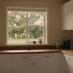 Renovated cottage kitchen with white cabinetry, timber bench and a window onto a green garden